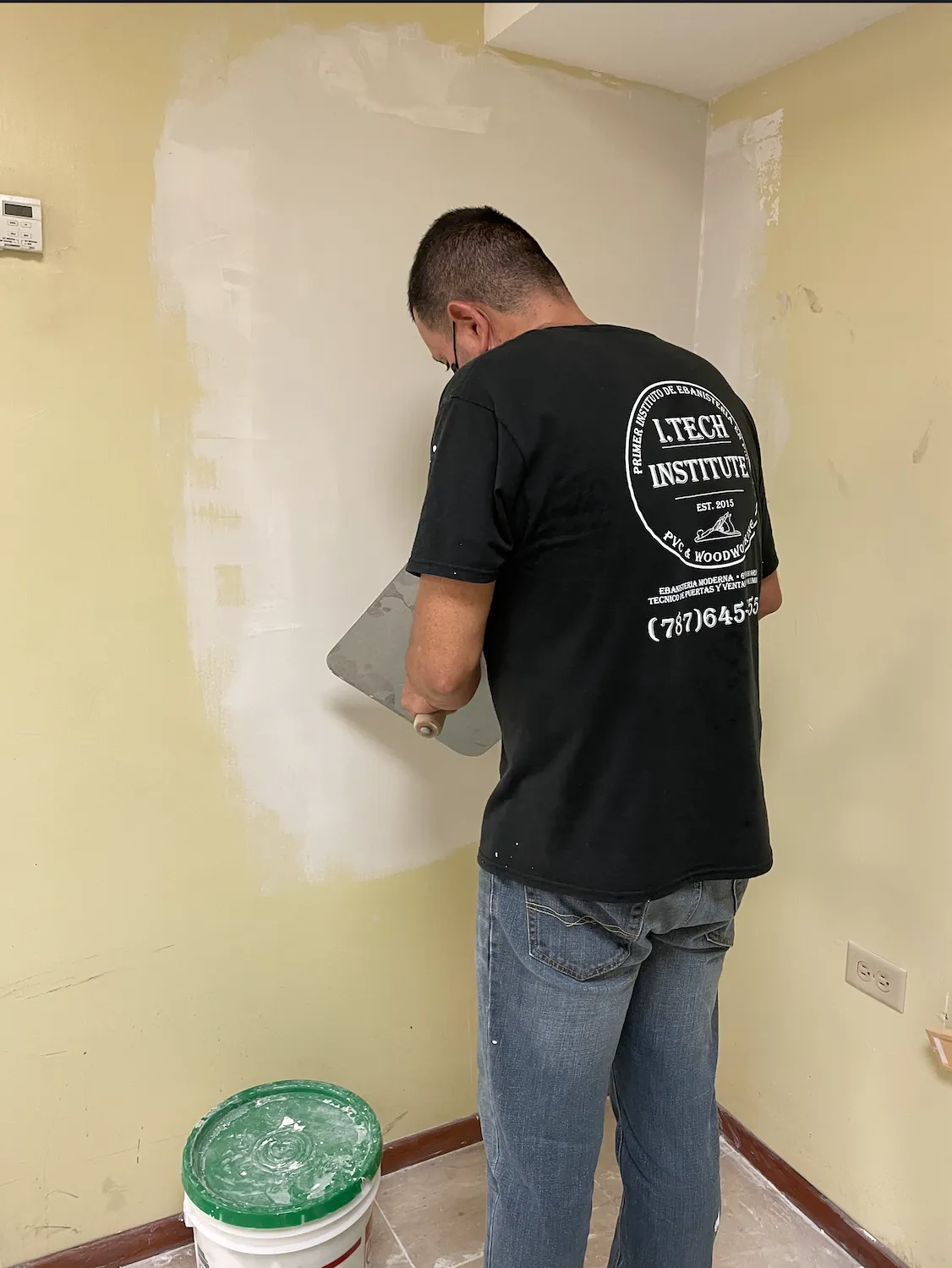 Estudiante aplicando masilla en una pared de gypsum board.