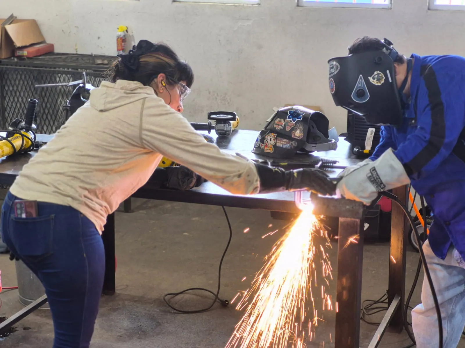 Estudiante cortando metal mientras el instructor supervisa.
